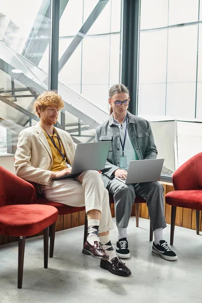 stock image two concentrated men working on their laptops together with window on backdrop, coworking concept