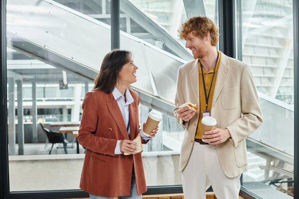 young colleagues enjoying lunch break and smiling at each other with glass on backdrop, coworking