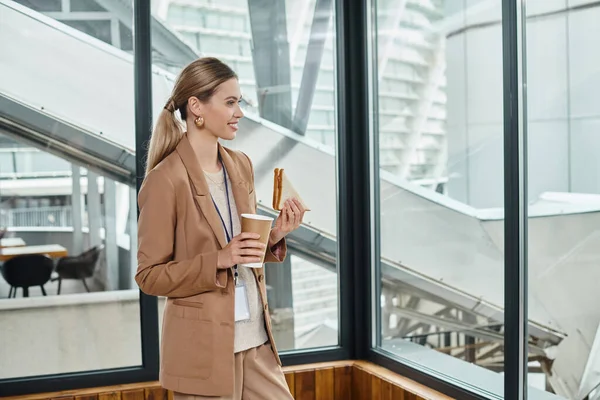 幸せなブロンドの女性は 仕事でランチ休憩中に彼女のサンドイッチとコーヒーを楽しんで コワーキングコンセプト — ストック写真