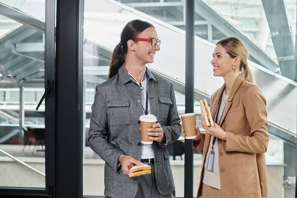 stylish team members having lunch break with sandwiches and coffee with glass backdrop, coworking