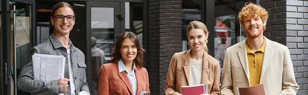 stock image cheerful young team posing outside with paperwork and smiling at camera, coworking concept, banner