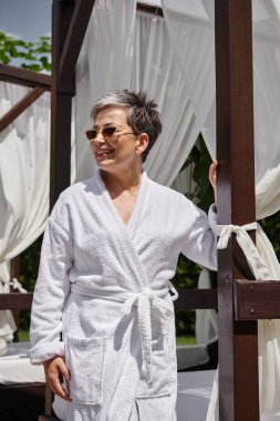 Güneş gözlüklü mutlu bir kadın özel bir köşkte dinleniyor, lüks bir tatil köyünde huzur içinde dinleniyor.