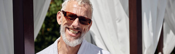 cheerful mature man in sunglasses and robe looking at camera during retreat in resort, banner