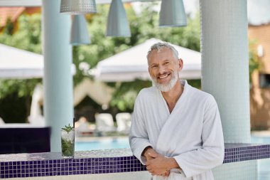 Beyaz cüppeli neşeli olgun bir adam barın yanında mojito kokteyli içiyor, geri çekiliyor.