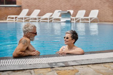 Güneş gözlüklü mutlu çift tatil sırasında havuz içinde sohbet ediyorlar, sağlık inzivası.