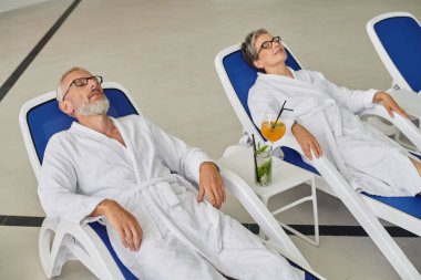 Geri çekilme kavramı, beyaz cüppeli olgun bir çift spa merkezindeki kokteyllerin yanında dinleniyor.