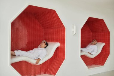 Spa inziva konsepti, beyaz cüppeli ve gözlüklü, dinlenme odasında dinlenen olgun bir çift.
