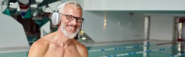 Memnun ve dövmeli olgun bir adam kablosuz kulaklıkla spa merkezinde müzik dinliyor.