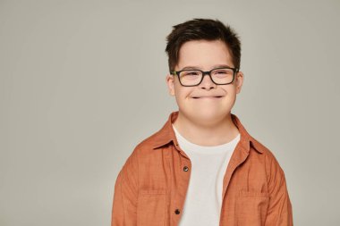 portrait of joyful boy with intellectual disability, in shirt and eyeglasses smiling on grey clipart