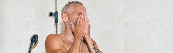 middle aged and shirtless man with tattoos taking shower and washing face, personal hygiene, banner