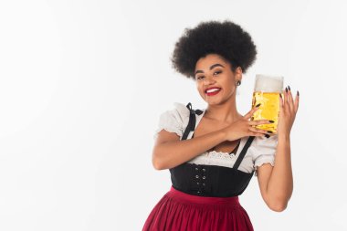 Oktoberfest kıyafetli neşeli Afro-Amerikan garson elinde köpüklü bir bardak bira tutuyor.