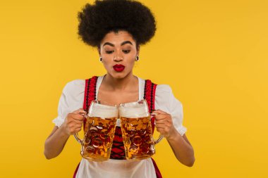 Genç Afro-Amerikan Ekim Festivali garsonu Bavyera kostümüyle bardakları sarıya tıkırdatıyor.