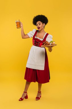 Afro-Amerikan Bavyera garsonu Dirndl 'de bira ve yemek ile sarı tepside poz veriyor.