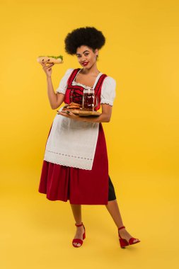 Neşeli Afro-Amerikan Oktoberfest garsonu bira ve lezzetli bir ikram ile sarı tepside.