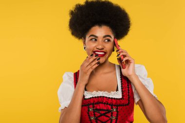 Geleneksel Ekim Festivali kıyafetleri içinde neşeli Afro-Amerikalı garson sarı telefonda akıllı telefondan konuşuyor.