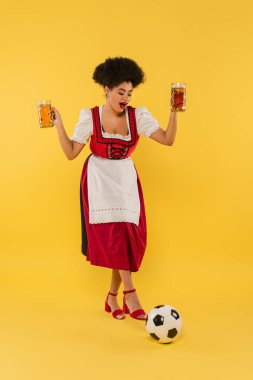 Neşeli Afro-Amerikan Bavyera garsonu Dirndl 'de elinde bira bardaklarıyla sarı top oynuyordu.