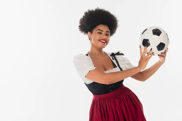 joyful octoberfest waitress in bavarian costume holding soccer ball african american on white