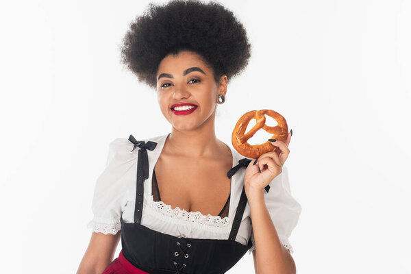 young african american waitress in traditional bavarian costume holding delicious pretzel on white