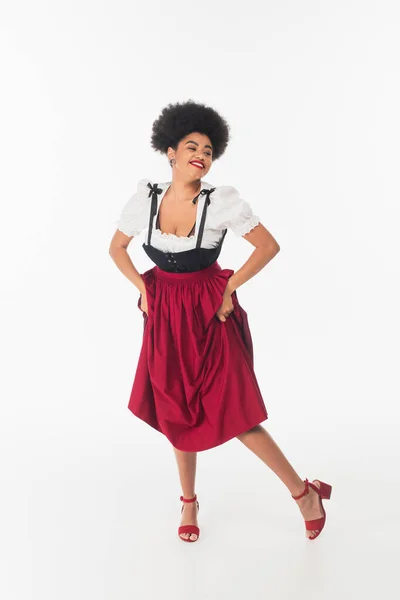 stock image overjoyed african american oktoberfest waitress in traditional bavarian costume dancing on white