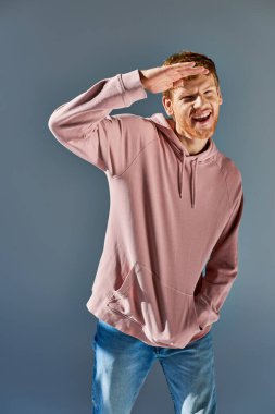 Moda kapüşonlu ve kot pantolonlu neşeli genç adam gri zeminde el ele poz veriyor.