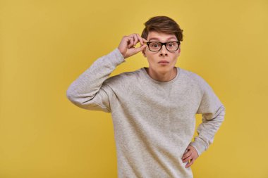 surprised young man in glasses and white casual sweatshirt touching his glasses looking at camera clipart