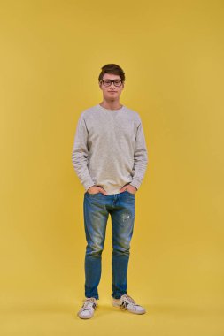 Kazaklı ve kot pantolonlu genç, yakışıklı bir adam elleri ceplerinde kameraya bakıyor.