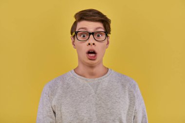 surprised young man in casual comfortable attire and glasses looking at camera with open mouth clipart