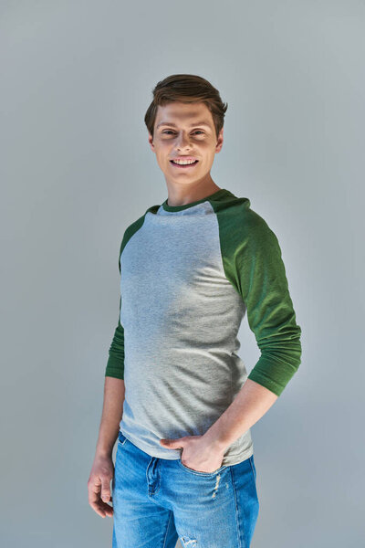 stylish young man in casual street wear standing and smiling at camera posing on grey backdrop