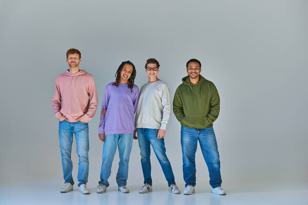 четыре веселые молодые люди в уличных повседневных нарядах глядя и улыбаясь в камеру, культурное разнообразие