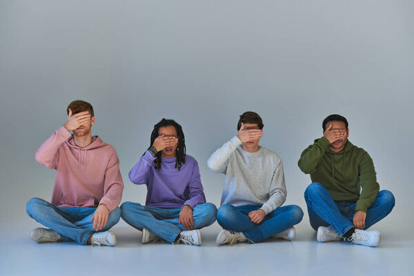 multicultural men in trendy outfits sitting with crossed legs covering eyes with hands, diversity