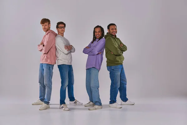 four young men standing back to back and smiling at camera on grey backdrop, cultural diversity