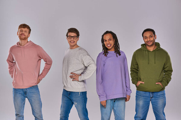 молодые многорасовые друзья в повседневной одежде стоя с руками акимбо на сером фоне, разнообразие