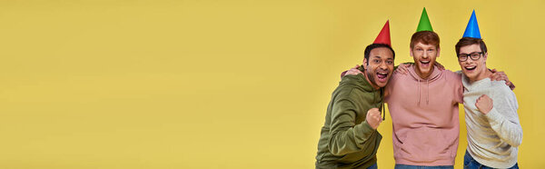 multicultural happy friends in casual attire with birthday hats looking at camera, birthday, banner