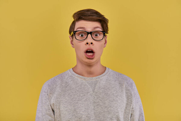surprised young man in casual comfortable attire and glasses looking at camera with open mouth