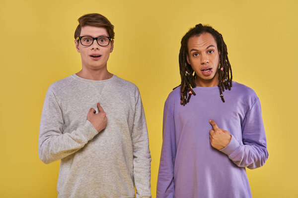 two young multiethnic friends looking puzzled confused pointing to themselves, cultural diverse