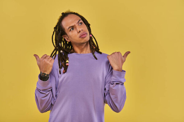 confused and puzzled young man with his thumbs pointing different ways on yellow background