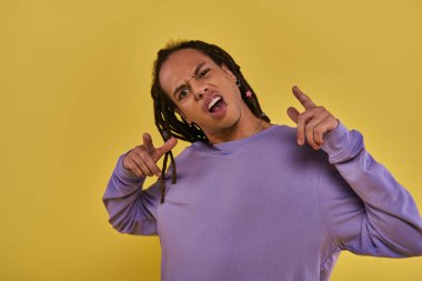 puzzled and surprised african american man in purple sweatshirt with dreadlocks pointing fingers clipart