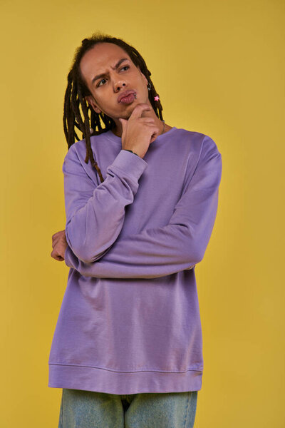 thoughtful young man in purple sweatshirt thinking and looking up and away on yellow background