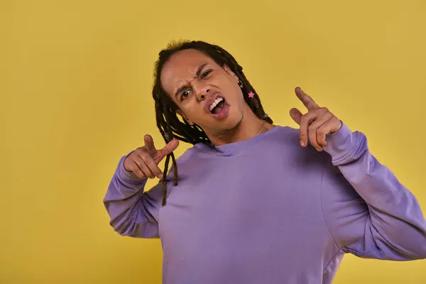 puzzled and surprised african american man in purple sweatshirt with dreadlocks pointing fingers
