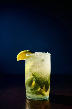 Nane ve koyu arkaplanda limon dilimleri ile süslenmiş taze mojito bardağı.