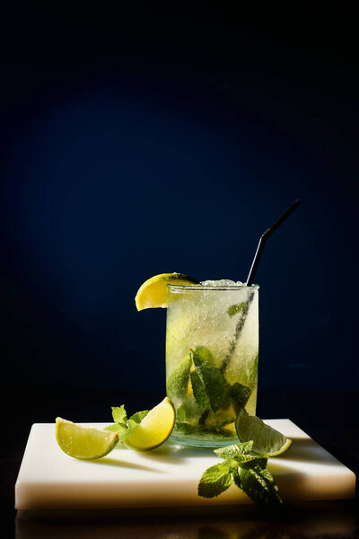 thirst quenching cold mojito garnished with mint leaves and lime on black backdrop, concept
