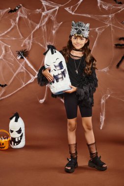 smiley preteen girl holds Halloween lantern on brown backdrop with web, spiders and bats, Halloween clipart