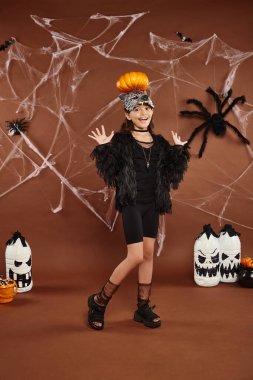 preteen girl holding pumpkin on her head with raised hands, brown backdrop with web, Halloween clipart