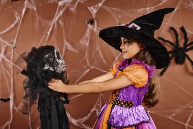 close up preteen kid holding spooky toy and looking at it, brown backdrop, Halloween concept clipart