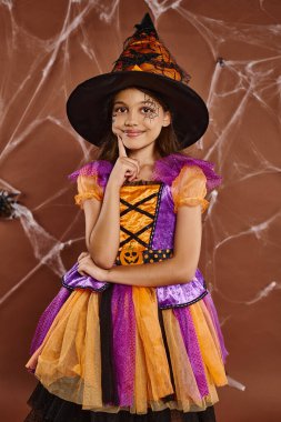 Cadı şapkalı mutlu kız ve Cadılar Bayramı kostümü Kahverengi arkaplanda örümcek ağları, ürkütücü sezon