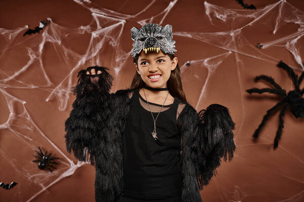 close up of preteen girl in black attire and wolf mask scaring with raised hands, Halloween concept