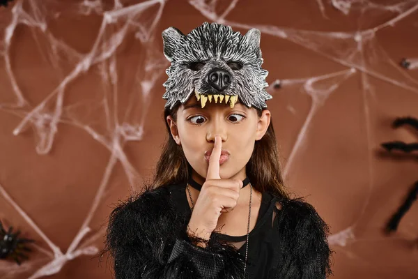 stock image close up preadolescent girl in wolf mask showing hush and looking at finger, Halloween concept