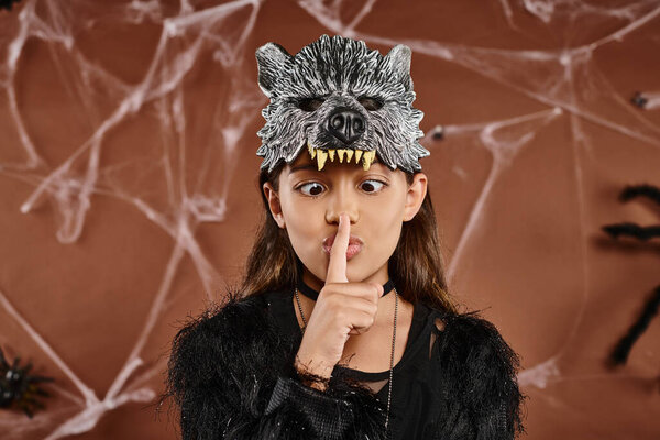 close up preadolescent girl in wolf mask showing hush and looking at finger, Halloween concept