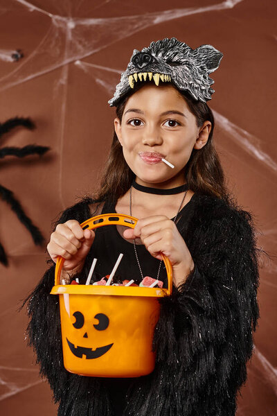 portrait of jolly girl with lollipop and bucket of sweets, Halloween concept, close up