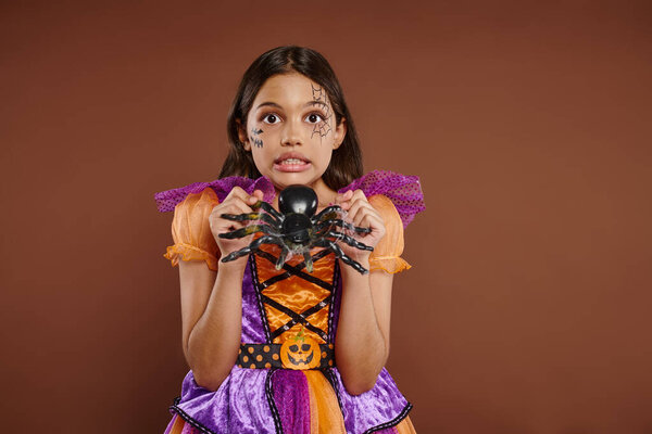 жуткая девушка в костюме Хэллоуина с фальшивым пауком и гримасой на коричневом фоне, 31 октября